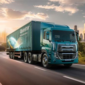 Groen vragmotor ry op ‘n rustige pad met stad se wolkekrabbers in die agtergrond.