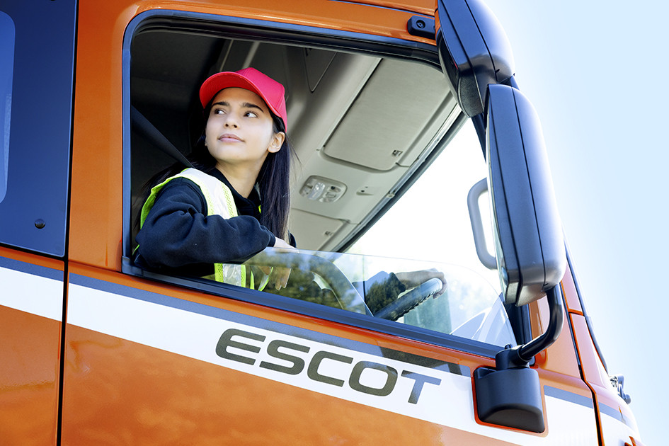Woman in red cap and safety vest driving an orange truck labeled ESCOT.