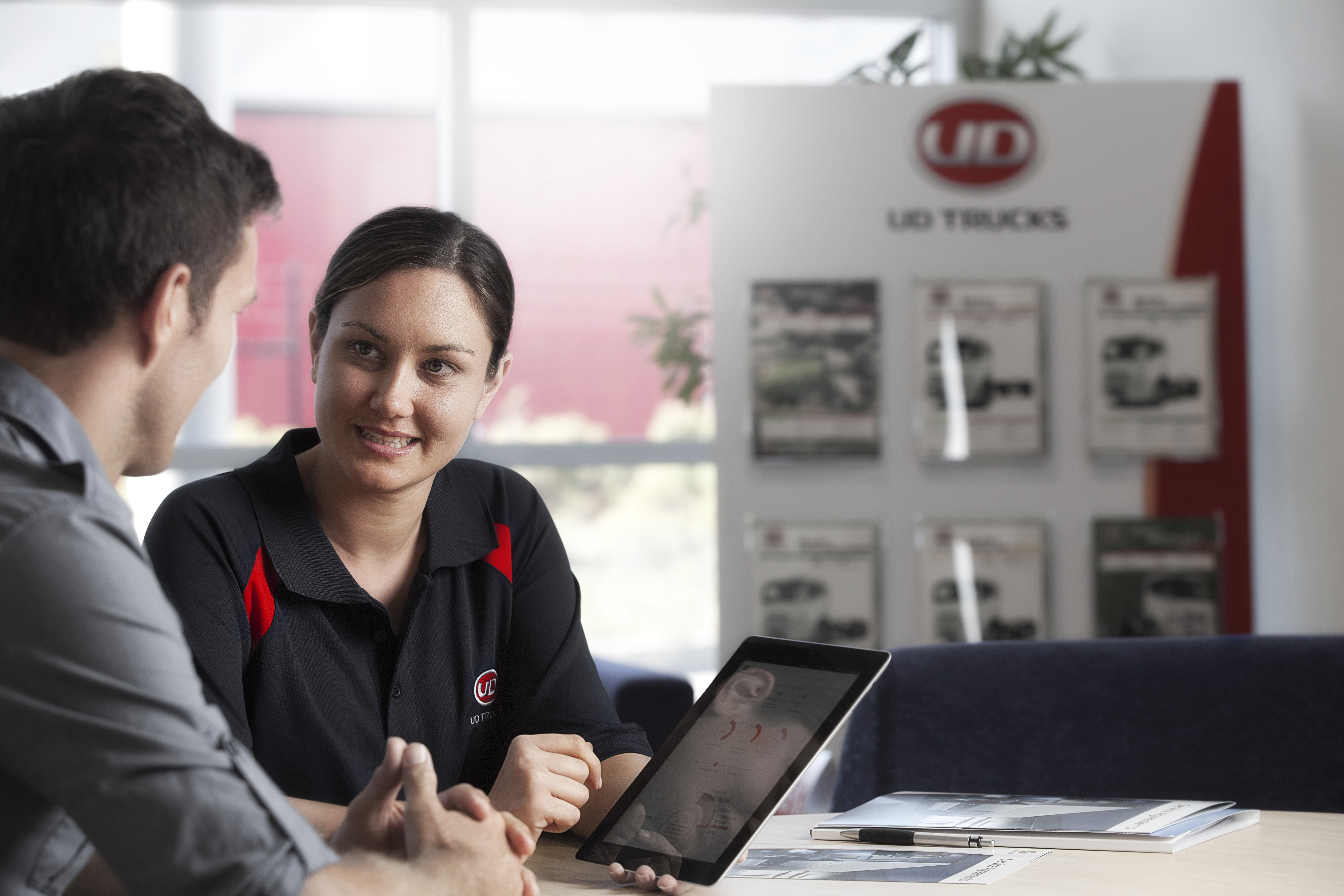 Two people discuss UD Trucks service plans at a desk with a tablet, 