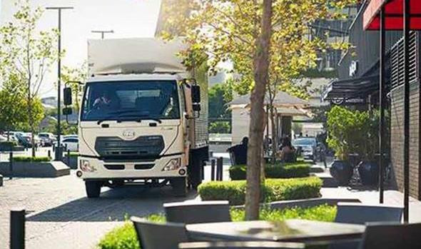 Delivery truck parked on a sunny city street near outdoor café tables.