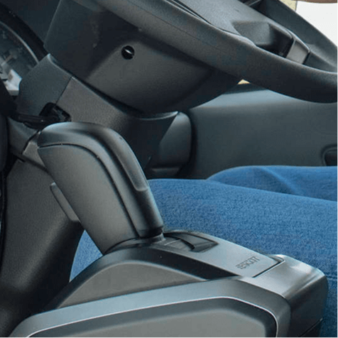 Tuas persneling otomatis mobil dekat setir dan kaki pengemudi berpakaian biru.