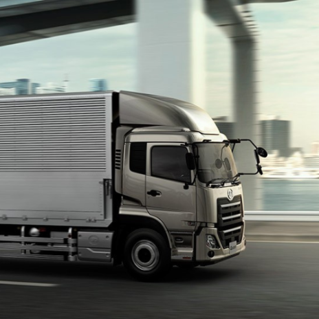 Silver truck driving on city road under a bridge with blurred background.