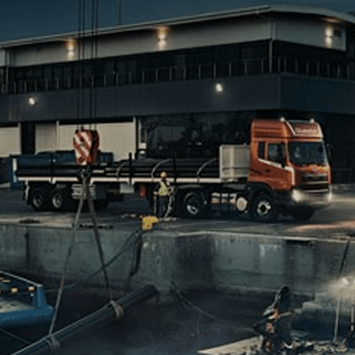 Trak sa konstruksyon site sa gabi, ilaw naka-on, may gusali sa likod.