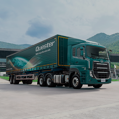 รถบรรทุกสีเขียวจอดหน้าอาคาร มีภูเขาเป็นฉากหลัง