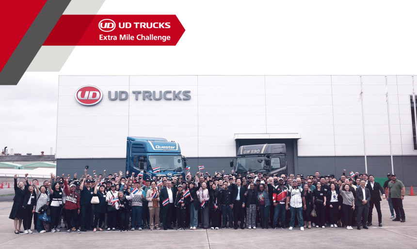 Large group of people posing in front of two trucks at a UD Trucks building.