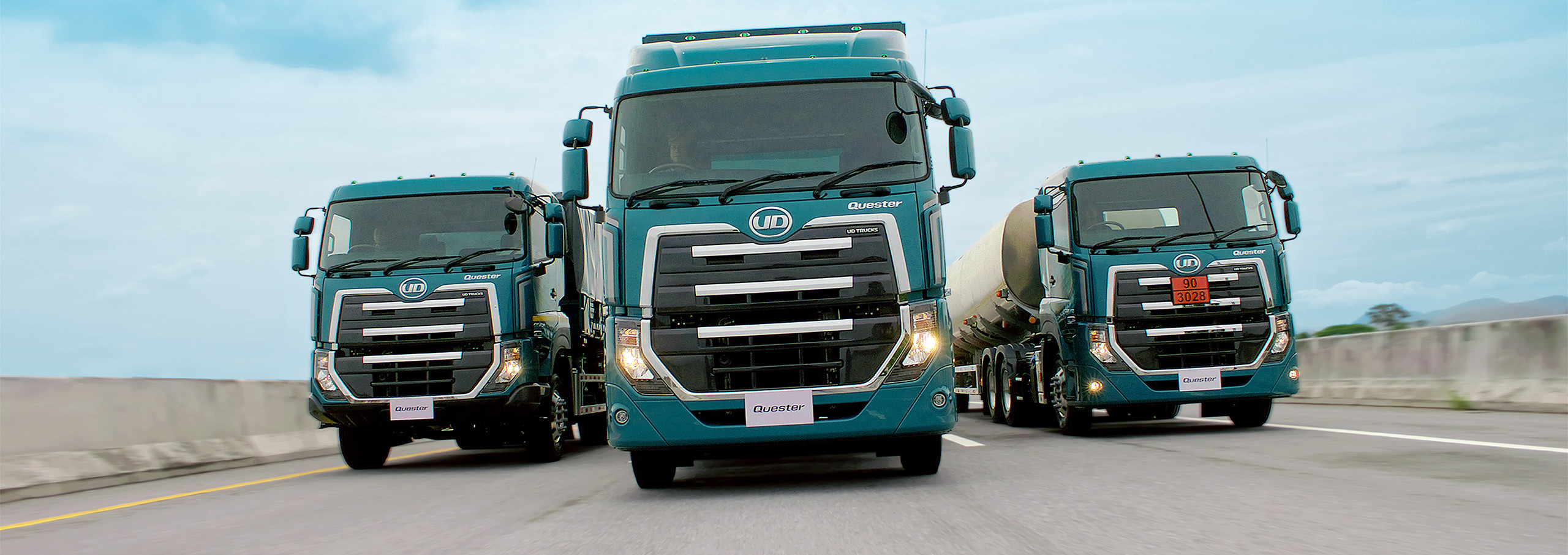 Three teal Quester driving side by side on a highway under a blue sky.