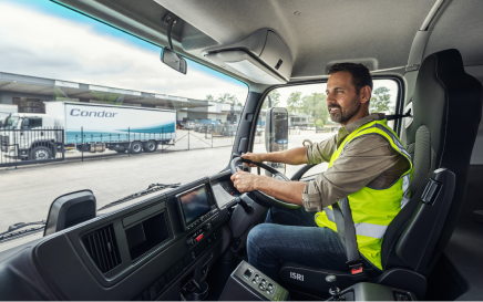 Man in hi-vis vest drives a truck, freight trucks and warehouse in background