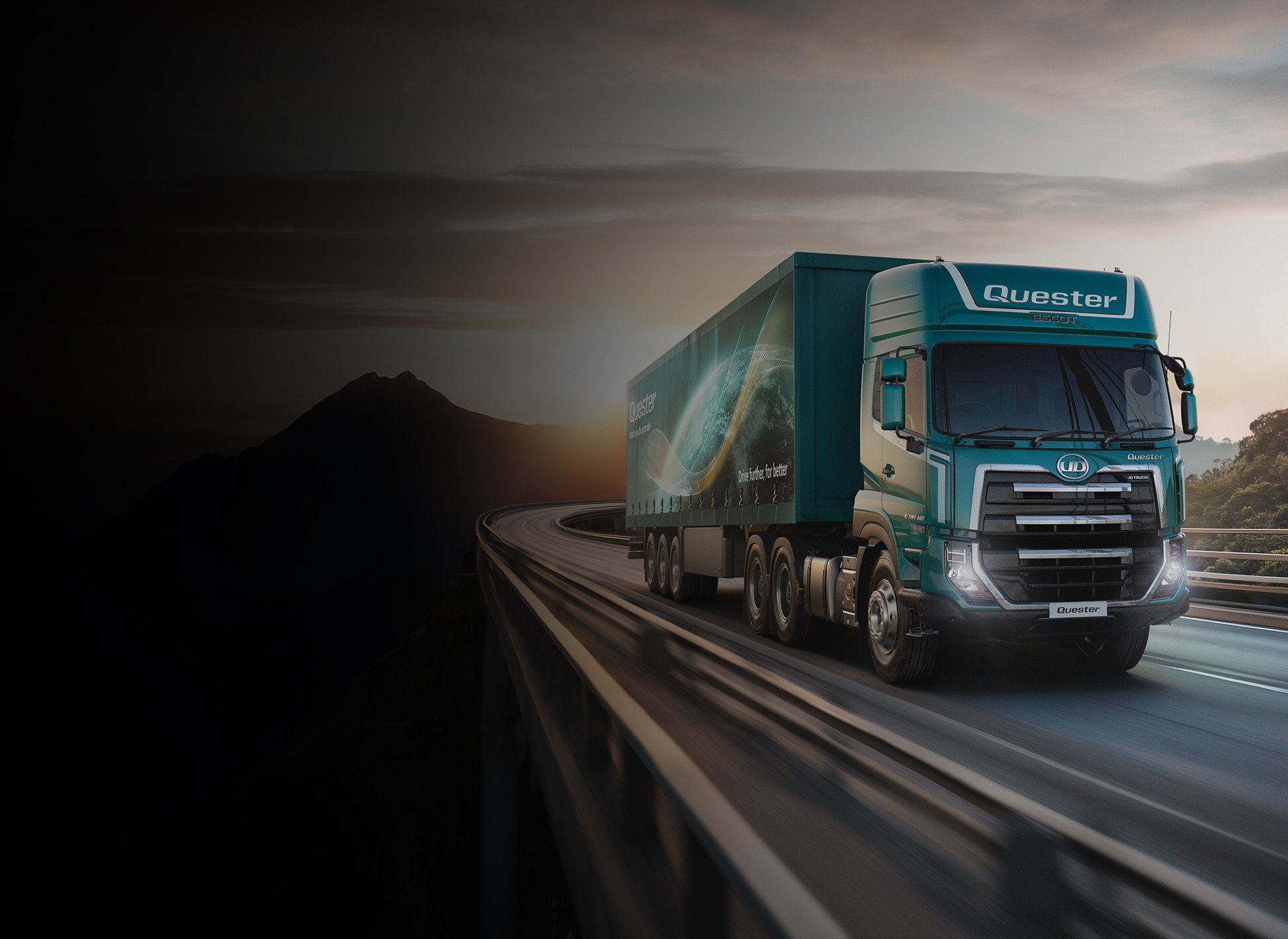 Green semi-truck driving on a highway at sunset with mountains in the background.