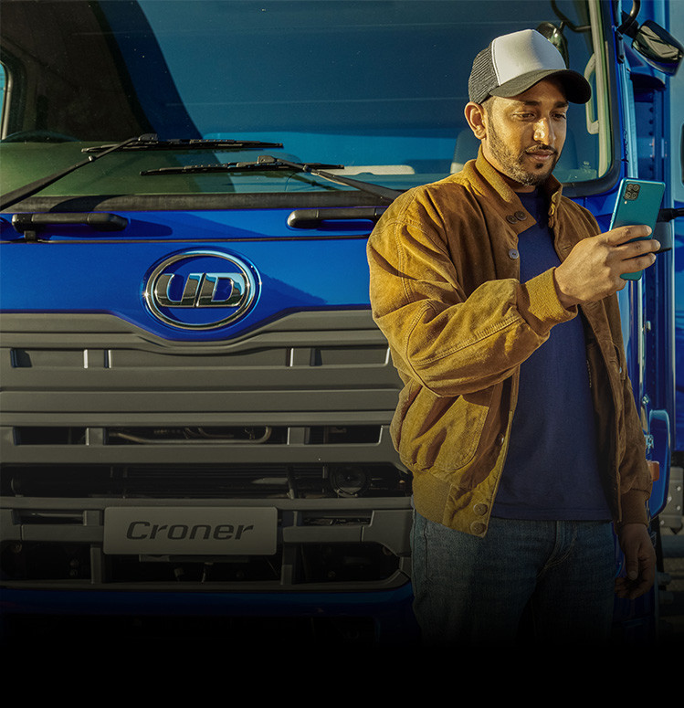 Man in brown jacket using a smartphone in front of a blue truck.