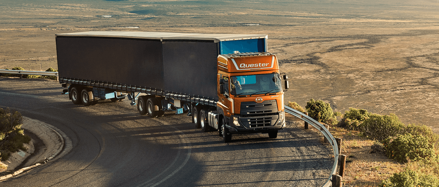 Lori oren jingga memandu di jalan berkelok di kawasan padang pasir.