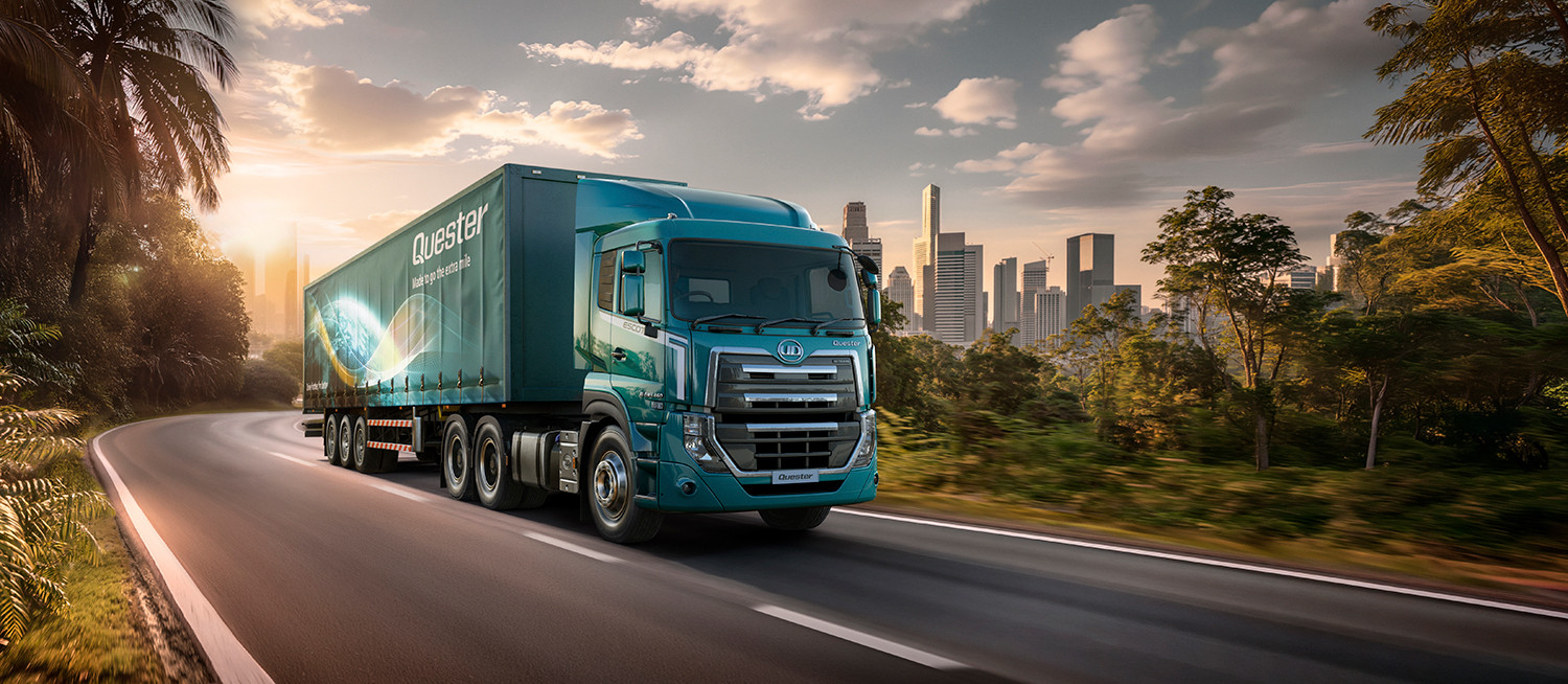 รถบรรทุกสีน้ำเงินวิ่งบนถนน ท่ามกลางธรรมชาติและเมืองใหญ่ยามเย็น